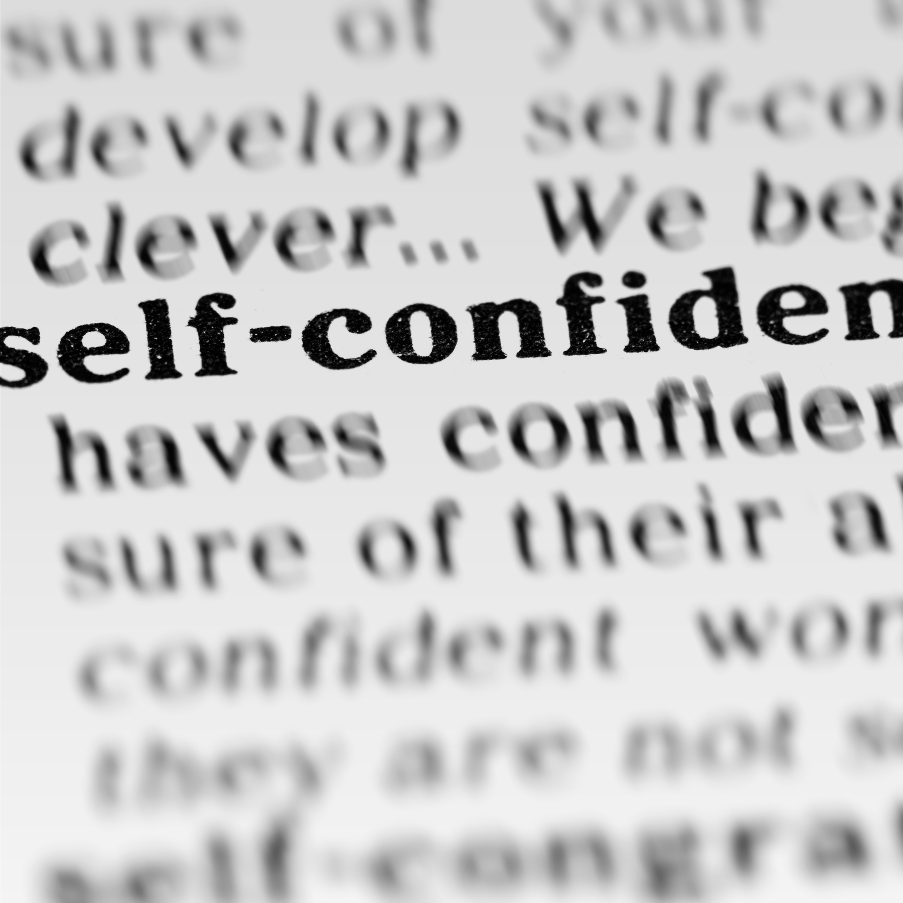 A close-up of a printed dictionary page with the word "self-confidence" in bold black text, sharply in focus, while the surrounding words are blurred.