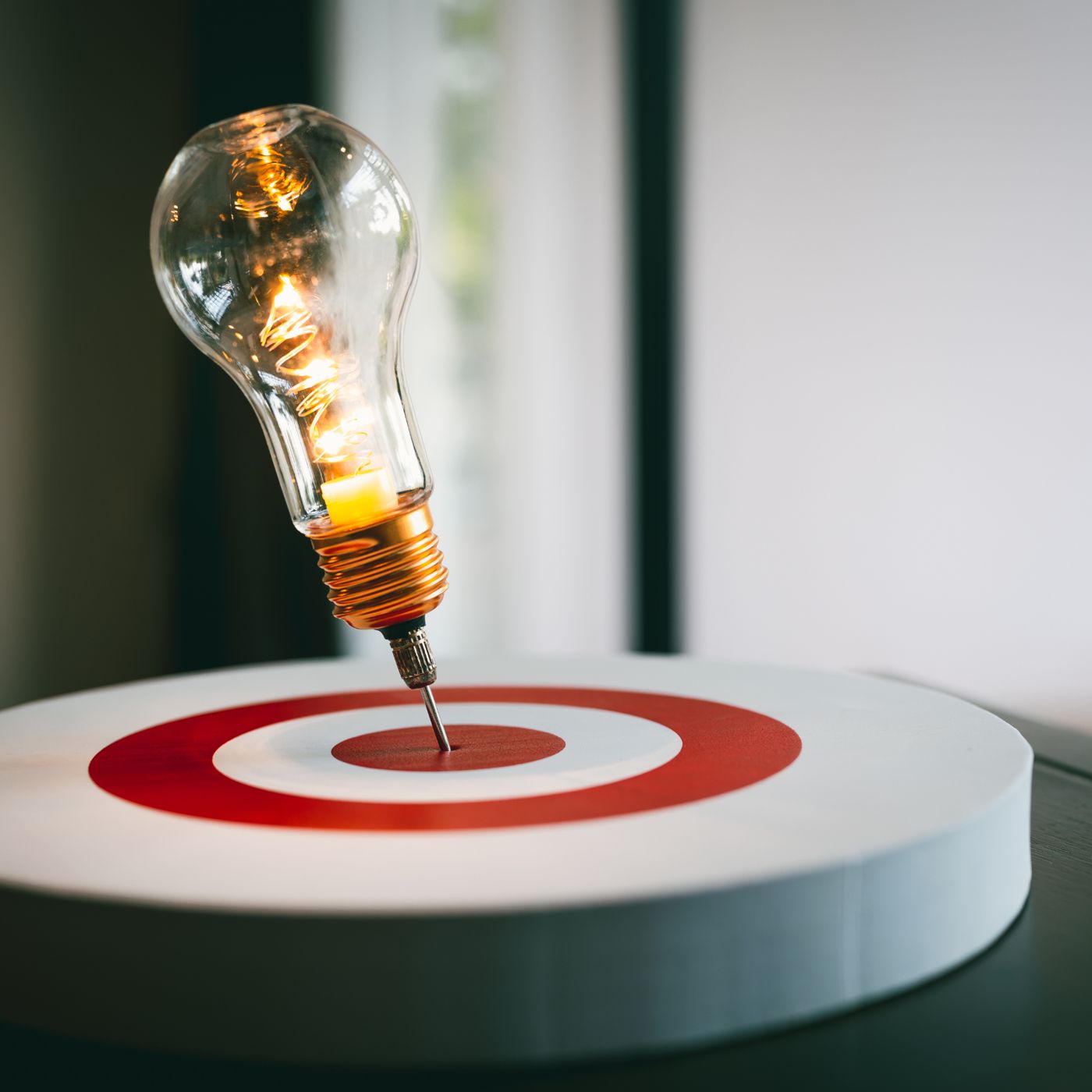 A glowing light bulb with its screw base piercing the bullseye of a red and white target, symbolizing innovation and precision.