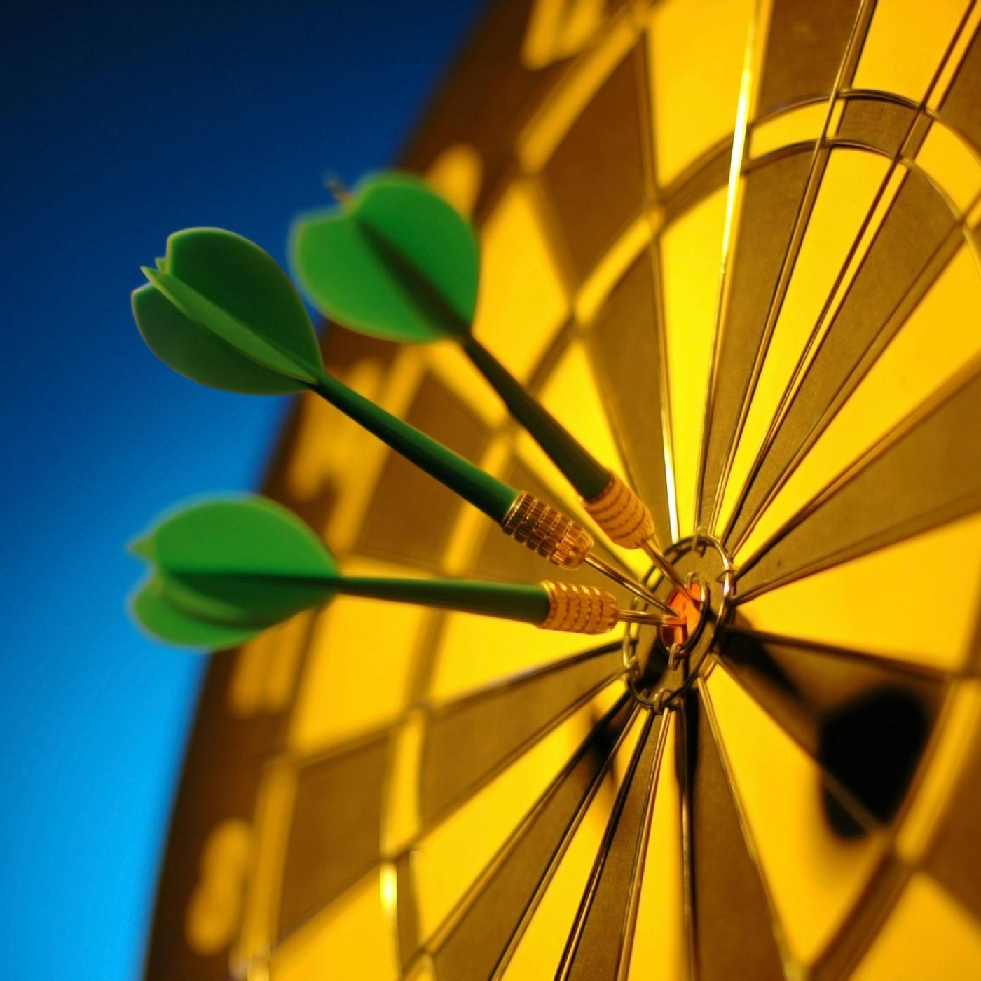Close-up of a dartboard with three green darts hitting the bullseye, symbolizing precision and success against a blue and yellow background.